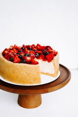 Delicious cheesecake topped with strawberries and blueberries on a wooden pedestal