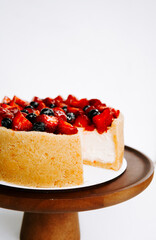 Delicious cheesecake topped with fresh berries arranged on a wooden cake stand