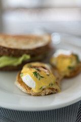 A beautifully plated eggs Benedict a perfectly poached egg sitting a top bacon and a toasted English muffin, generously drizzled with rich hollandaise sauce