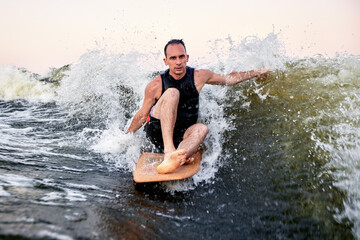 Man surfing on wave with wooden board during vibrant sunset