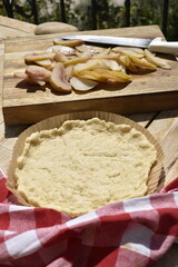 A sheet of raw dough in a round paper mold on a wooden background and sliced pears, top view