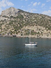 A white yacht anchored in a serene bay at the foot of a majestic mountain. Ideal for travel, adventure, luxury lifestyle, and sailing concepts.