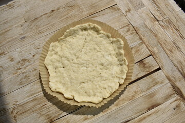A sheet of raw dough in a round paper mold on a wooden background, top view