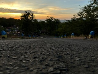 Countryside downhill road with textured surface under warm golden sunset sky in rural landscape.