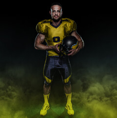 Intense male athlete in football gear, standing with helmet against dark background and smoke. Ideal for sports branding, magazine covers, web design and advertising.