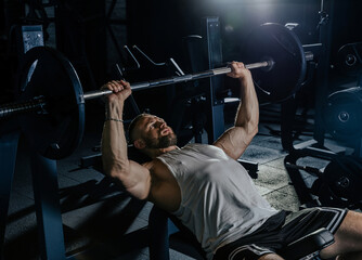 Muscular man training with weights. Brutal strong athletic men pumping up muscles workout in dark gym.