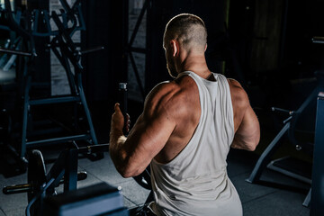 Muscular man training with weights. Brutal strong athletic men pumping up muscles workout in dark gym.