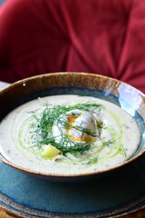 Close-up view of a traditional Czech soup Kulajda with mushrooms, egg, and potatoes, garnished with fresh dill. Served in a rustic style on a wooden table in a restaurant, showcasing authentic taste.
