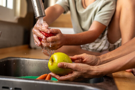 Close-up of child and adult washing fresh apples under running water in the kitchen sink - Powered by Adobe