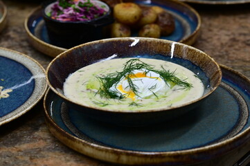 Close-up view of a traditional Czech soup Kulajda with mushrooms, egg, and potatoes, garnished with fresh dill. Served in a rustic style on a wooden table in a restaurant, showcasing authentic taste.