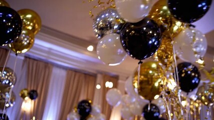 Celebration with elegant decorations featuring black, gold, and white balloons in a festively lit venue