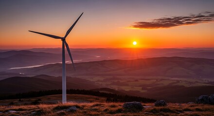 Fototapeta premium Wind turbine on a hill at sunset with mountains in the background and a bright orange sky above it all