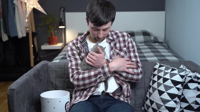A happy man receives a tiny grey kitten as a gift, tenderly hugging and petting his new furry friend. This heartwarming moment captures pure joy and the beginning of a beautiful bond
