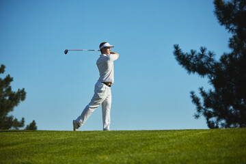 Golfer completing dynamic swing on sunny golf course. Concept of active lifestyle, motivation, physical discipline, leisure, and sports balance.