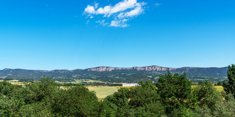 The vast beauty of Montsec in Catalonia, Spain. Views of vast blue skies, lush greenery and the distinct rocky ridges create a serene and picturesque landscape typical of the region.