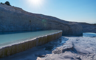 The stunning landscape of Pamukkale in Turkey features terraced travertine pools created by mineral-rich thermal waters. The bright white terraces contrast with the deep blue sky.