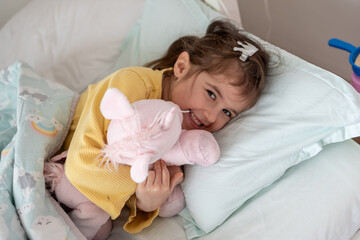 Morning awakening little child girl with her toy in bed. Happy girl in pajamas on bed right after awaking. Happy family concept