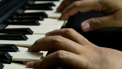 Fototapeta premium Pianist hands playing with both hands viewed from diagonal top angle, black piano with dark background, concept of concert, melody, art, and expressive performance.