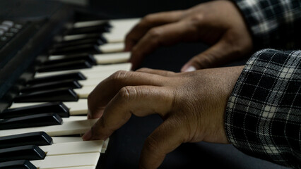 Fototapeta premium Pianist hands playing with both hands viewed from diagonal top angle, black piano with dark background, concept of concert, melody, art, and expressive performance.