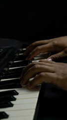 Fototapeta premium Piano played with two hands seen from slightly elevated diagonal angle in portrait orientation, dark setting, concept of creativity, art, harmony, and performance.