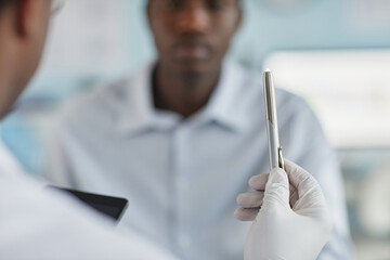Black man sitting in medical office focusing on pen held by gloved hand of healthcare professional during neurological examination, blurred background emphasizing clinical setting