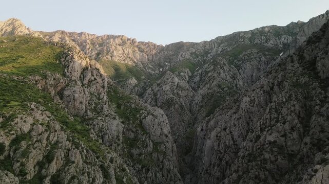 Late golden hour lights a serrated ridge above a hidden ravine in Uzbekistan. Fine detail in limestone wall and alpine grassland makes a strong nature backdrop for travel and storytelling