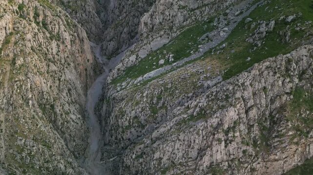 High perspective frames a vertical look down to a canyon floor and stream bed in Uzbekistan. Detail in gravel, rock and slope supports strong stock use for travel, geology and nature brand work