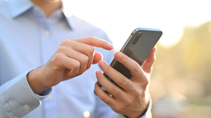 Fototapeta premium Close up of a person's hands using a smartphone outdoors with a soft bokeh background