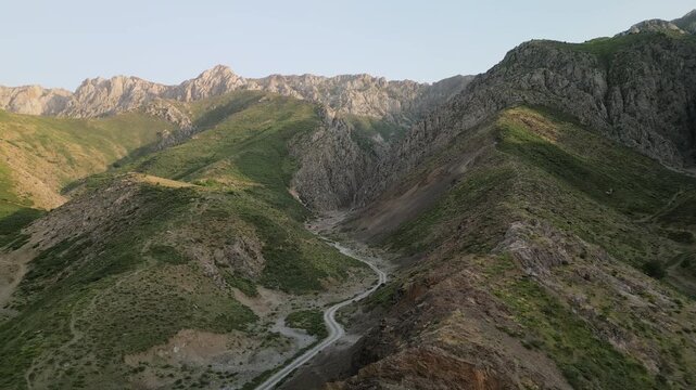 Golden morning light reveals a winding mountain road leading into a rocky gorge in Uzbekistan. Warm tones, clean air, and vast distance create a cinematic sense of scale and adventure