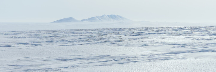 Arctic landscape. View of the snow-covered tundra and snow-capped mountains. Cold weather. The harsh climate of the polar region. Nature of the Arctic. Wide panorama. Great for background.