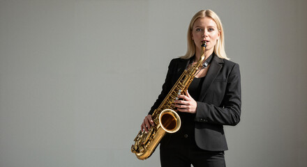Obraz premium Woman playing saxophone in black suit against gray background 