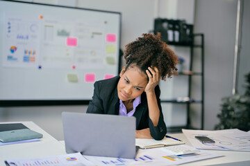 Stressed african american businesswoman looking at laptop in office with hand on head