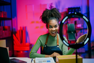 Young african american woman working at her startup small business, recording a video blog about...