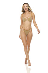 Fototapeta premium Front view of smiling blonde woman in golden lingerie walking barefoot. Studio shot on white background.