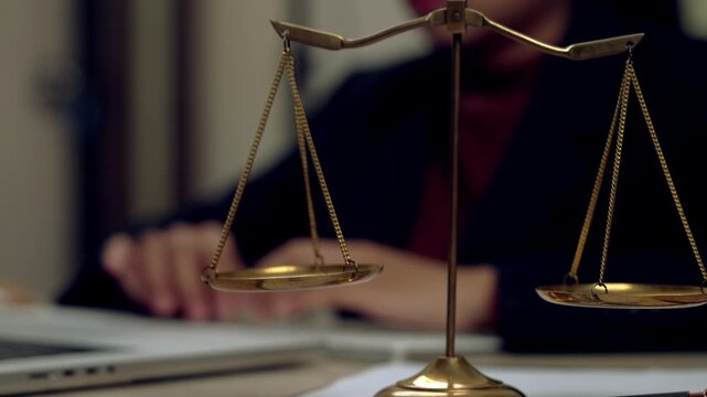 Close-up of golden balance scales symbolizing justice with a lawyer working in the background at a law office. Ideal for legal, law firm, or justice concept.