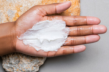Moisturizing cream applied on hand, showcasing smooth texture against natural stone background