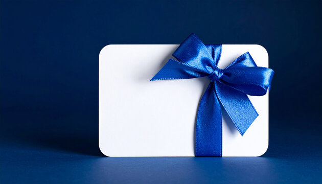 Glossy blue ribbon bow on white gift card against dark blue background. Mock-up. Close-up. - Powered by Adobe