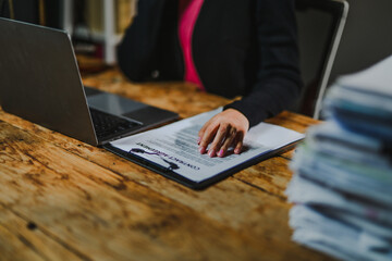 Businesswoman reviewing contract assessment with laptop on wooden desk