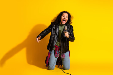 Attractive man in a leather jacket singing passionately with a microphone against a vibrant yellow background