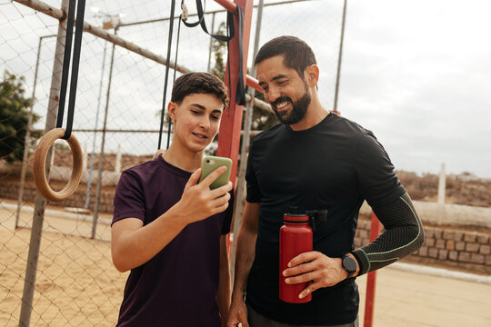 Teenage boy and adult man looking at a smartphone together at an outdoor gym