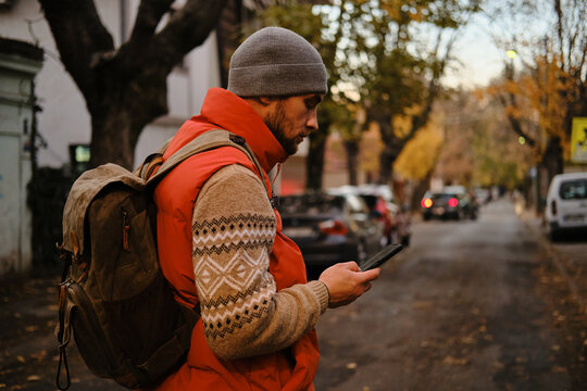 Man with backpack looking at phone on autumn street, Belgrade