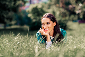 Relaxed young woman lying in a sunny urban park with a cheerful expression enjoying leisure time outdoors in casual attire
