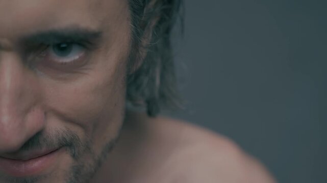 Evil, beautiful, cunning man-serpent: Close-up of a young handsome Slavic man with fair skin revealing emotional depth through intense gaze and subtle smirk against a muted gray background.