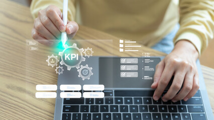 Close-up of a hand using a digital pen on a laptop with a hologram interface showing KPI, business performance metrics, data analytics, and a management dashboard for strategic planning.
