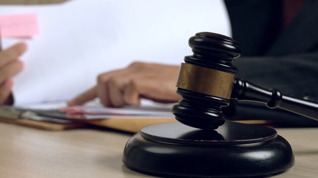 Close-up of judge gavel on desk with blurred lawyer handling documents in background, symbolizing legal authority, justice, and court decision.