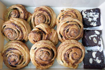 Fototapeta premium Appetizing assortment of freshly baked cinnamon swirl pastries and decadent chocolate brownies, neatly arranged white box. Golden brown spirals and rich fudgy squares offer satisfying dessert