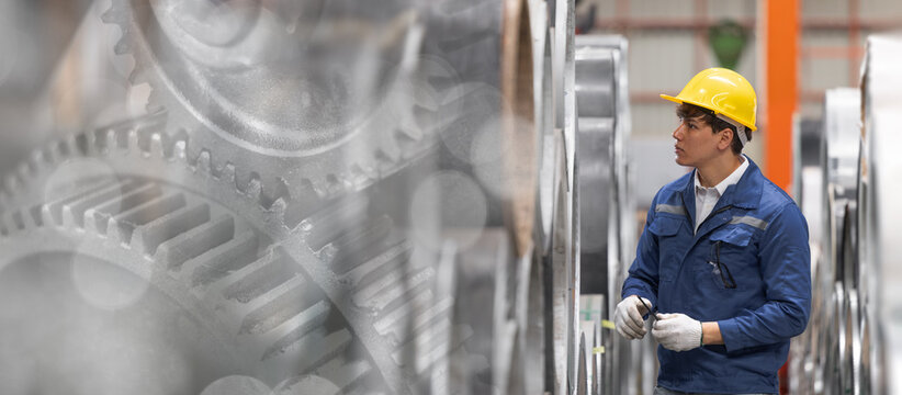 Industrial worker in blue uniform and yellow safety helmet inspecting machinery at factory banner