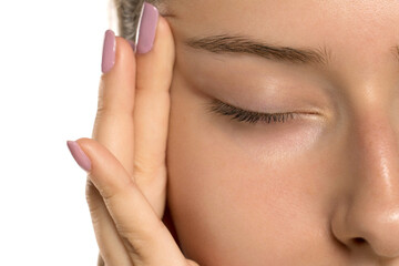Studio shot extreme closeup of young woman with closed eye touching skin near temple on white background. © vladimirfloyd