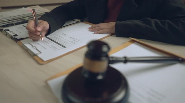 Close-up of lawyer signing legal documents at desk with judge gavel. Professional legal advisor or attorney at work in law office.
