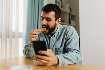 Man having a snack and using phone in cozy living room